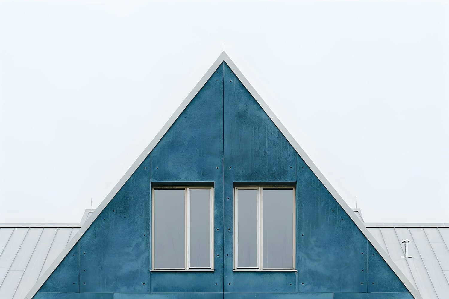 Steep gable with standing seam metal roof panels against a pale sky
